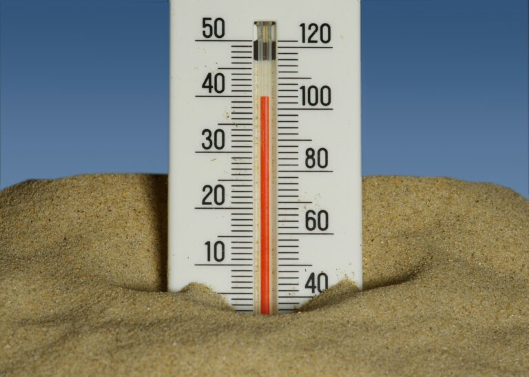 a thermometer reading 102 degrees sticks out of the sand.