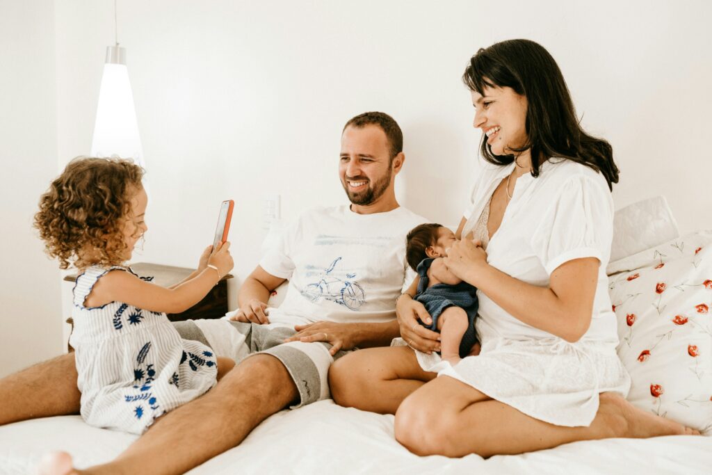 A Family smiing and hanging out on a bed.